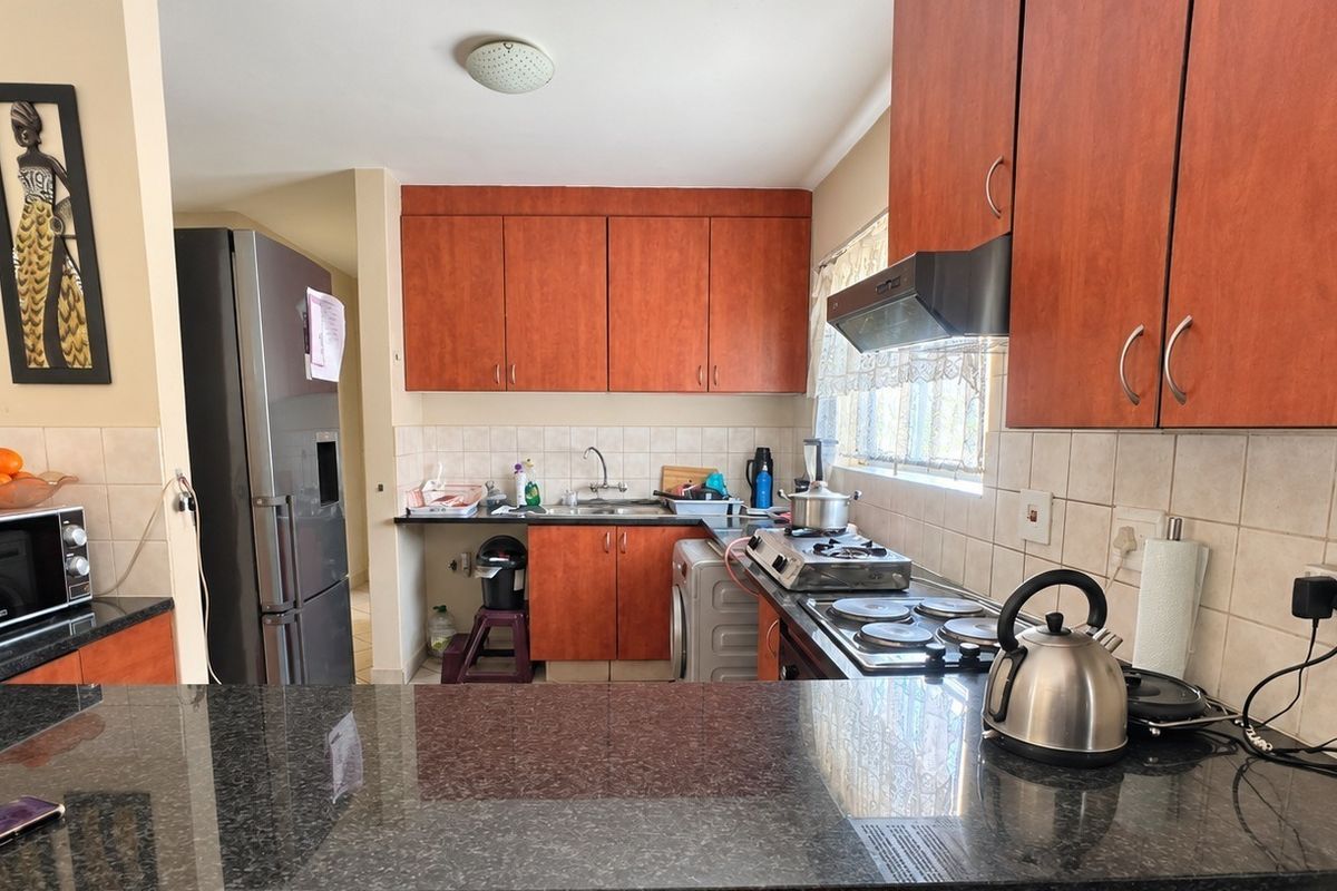 A functional kitchen featuring granite countertops, wood-finish cabinetry, a built-in hob, and an extractor fan, providing a practical workspace for daily cooking.