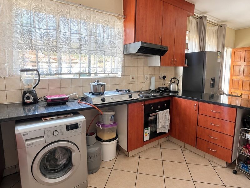 Functional kitchen featuring wood-finish cabinetry, granite countertops, gas hob, built-in oven, and tiled flooring with integrated laundry plumbing.