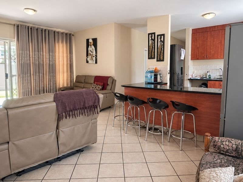 Open plan living and kitchen area featuring tiled flooring, a breakfast bar with granite countertops, and direct access to the patio through sliding doors.
