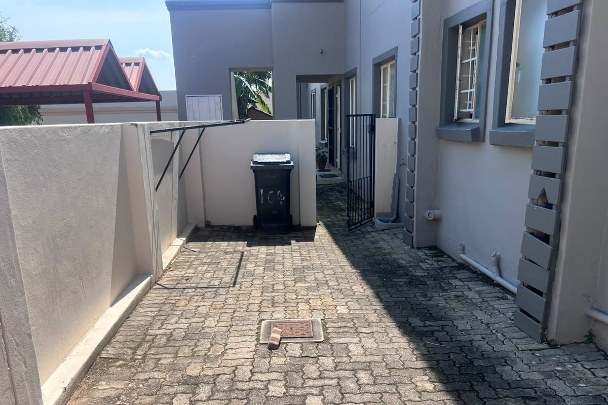 A paved rear courtyard area featuring boundary walls, a security gate, and external plumbing fixtures, showing signs of weathering and wear.