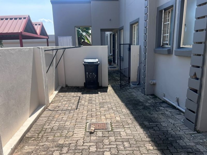 A paved rear courtyard area featuring boundary walls, a security gate, and external plumbing fixtures, showing signs of weathering and wear.