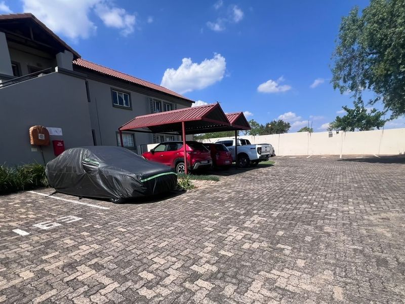 Exterior view of the townhouse complex featuring a paved parking area with covered carports and a secure perimeter wall.