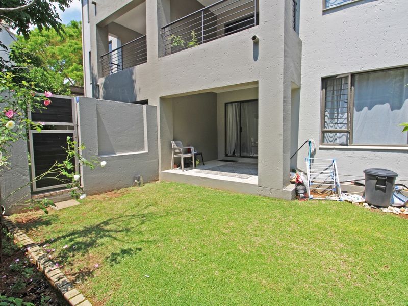 Rear view of the apartment featuring a private garden, a covered patio area, and a balcony with metal railings.