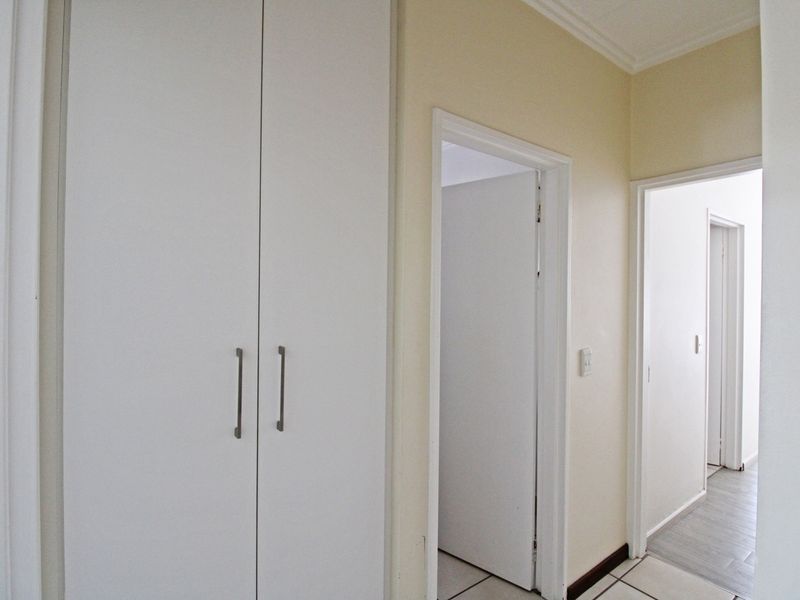 A clean, neutral hallway featuring built-in cupboards and tiled flooring, providing access to multiple rooms within the apartment.