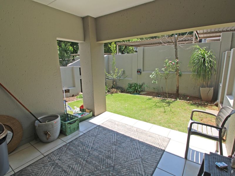 A covered patio area featuring tiled flooring and concrete pillars, opening onto a private garden with a lawn and boundary wall.