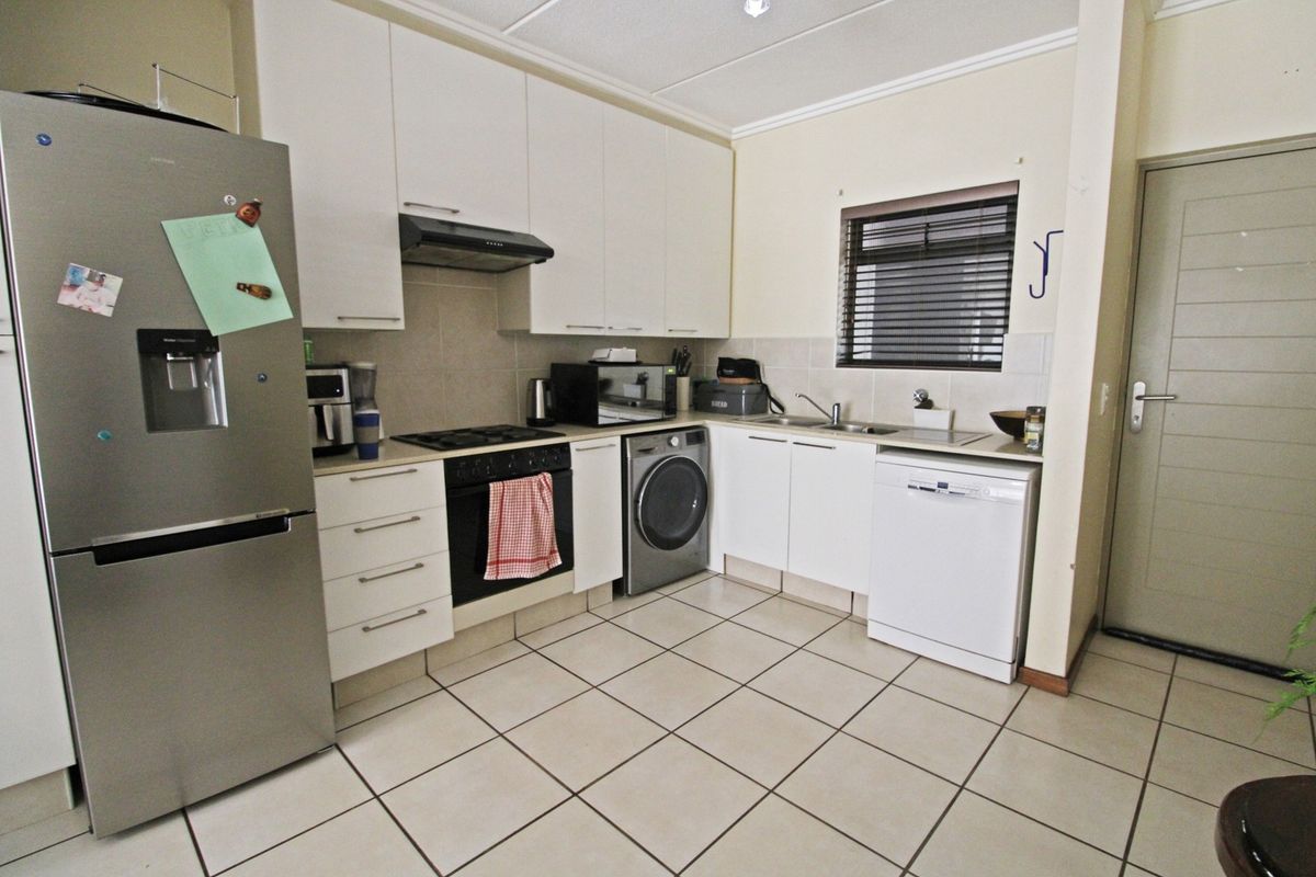 Functional kitchen featuring white cabinetry, tiled flooring, built-in oven with gas hob, extractor fan, and integrated space for laundry and dishwasher appliances.