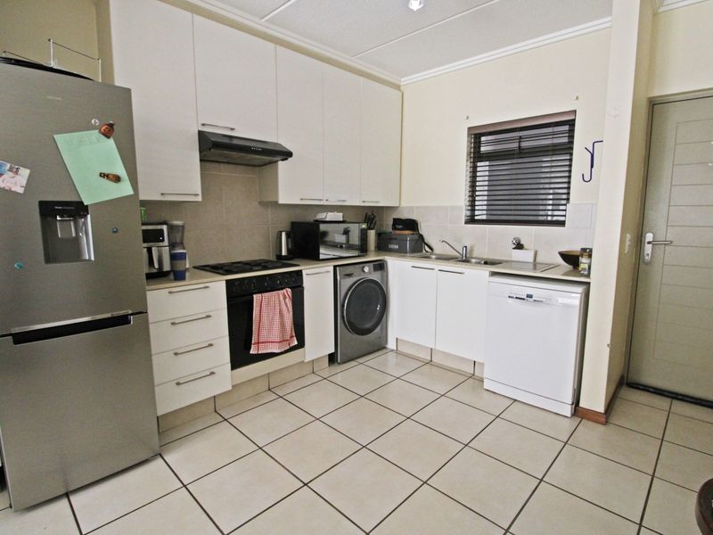 Functional kitchen featuring white cabinetry, tiled flooring, built-in oven with gas hob, extractor fan, and integrated space for laundry and dishwasher appliances.