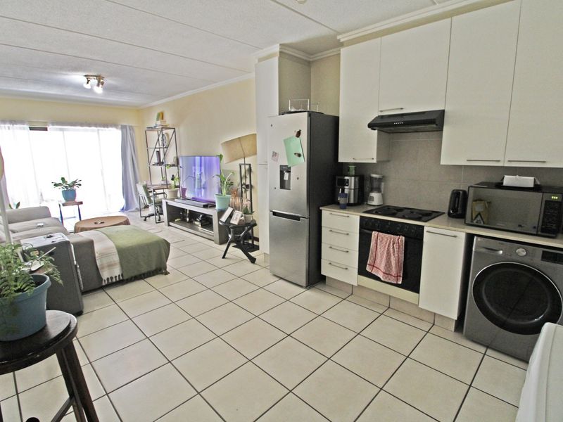 Open-plan living area featuring a functional kitchen with built-in cabinetry, oven, and hob, flowing into a bright lounge space with sliding door access.