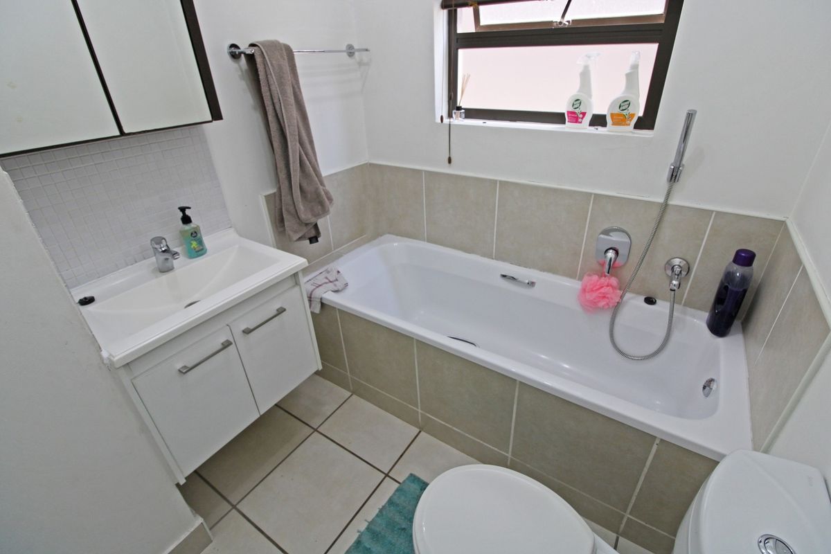 A functional bathroom featuring a white vanity with basin, a bathtub with shower mixer, and neutral wall and floor tiling.