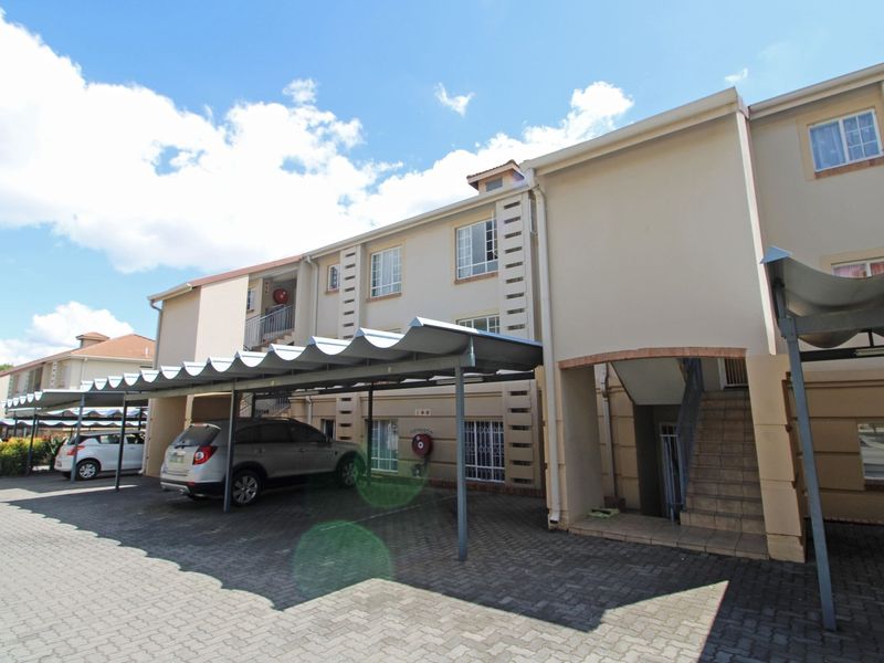 Exterior view of an apartment complex featuring covered parking bays, paved driveway, and external staircases providing access to upper levels.