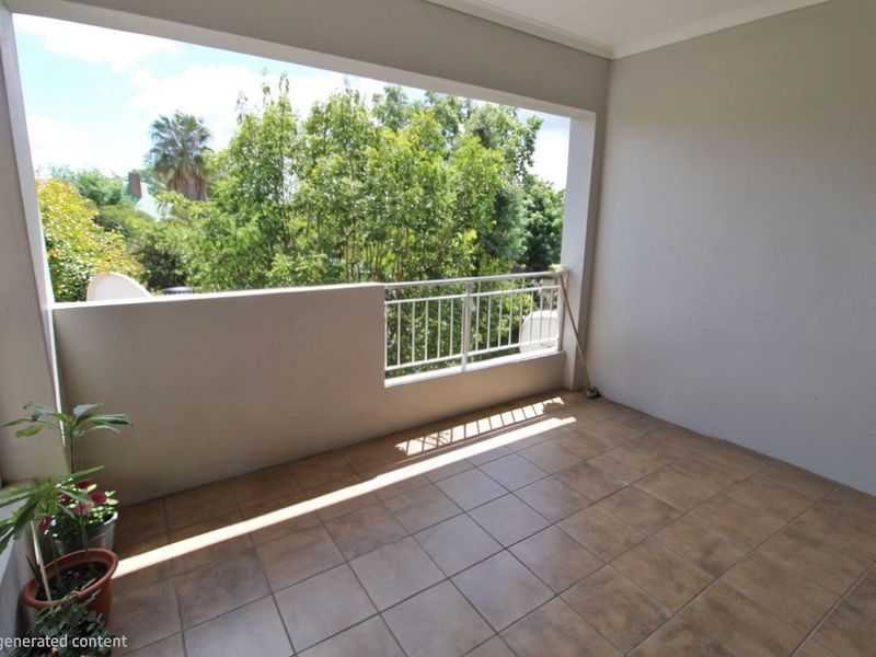 A spacious, covered balcony featuring tiled flooring and a metal balustrade, offering an open-air space with views of surrounding greenery.