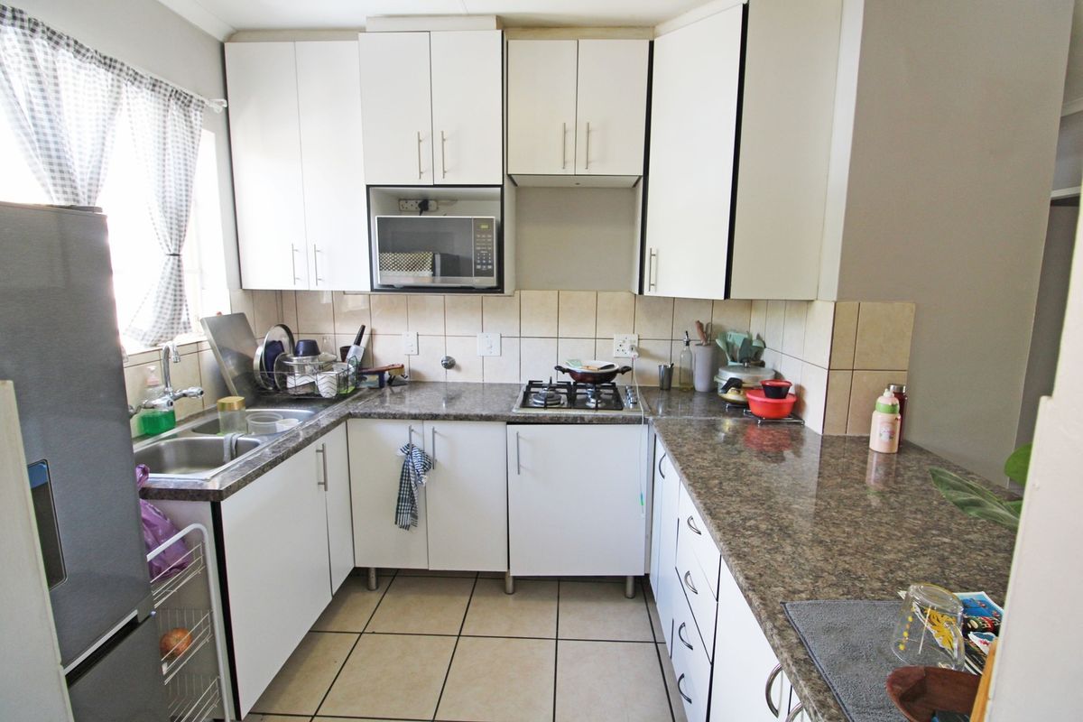 A functional kitchen featuring white cabinetry, granite countertops, a gas hob, built-in microwave, and tiled flooring with a neutral backsplash.