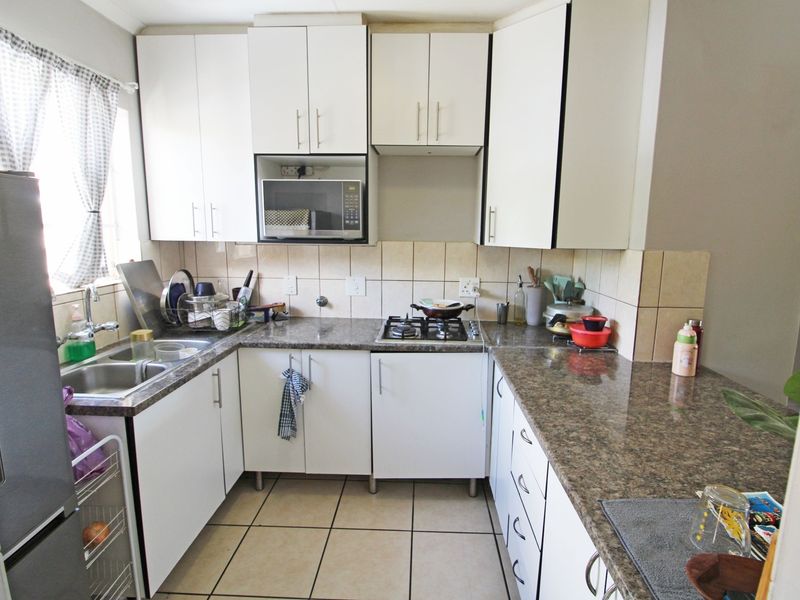 A functional kitchen featuring white cabinetry, granite countertops, a gas hob, built-in microwave, and tiled flooring with a neutral backsplash.