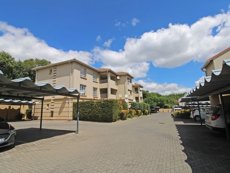 Exterior view of a multi-story apartment complex featuring paved driveway access and covered carport parking bays.
