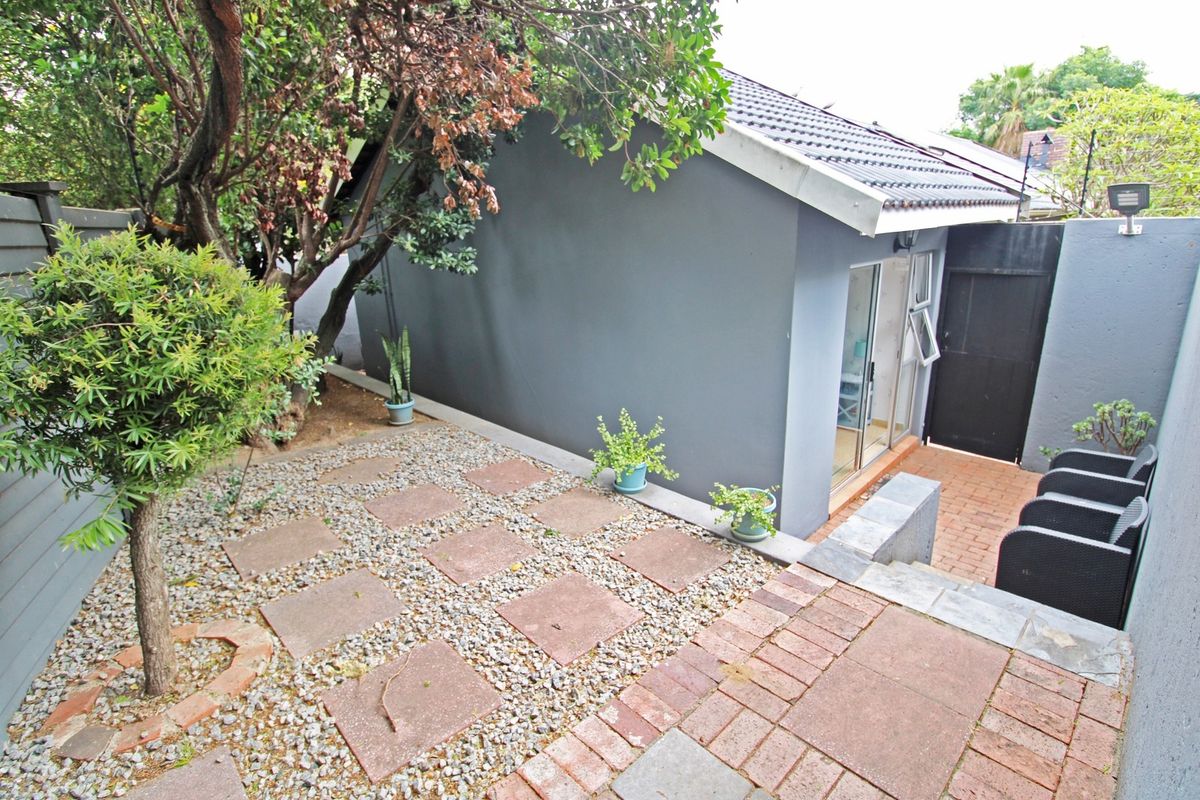 A rear exterior view of the cottage featuring a paved patio area, gravel garden section, and a sliding glass door entrance.