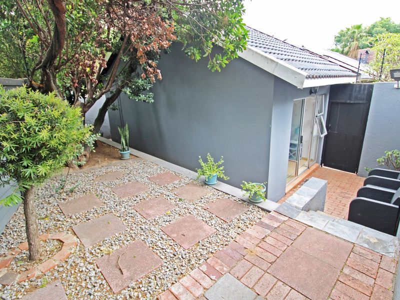 A rear exterior view of the cottage featuring a paved patio area, gravel garden section, and a sliding glass door entrance.