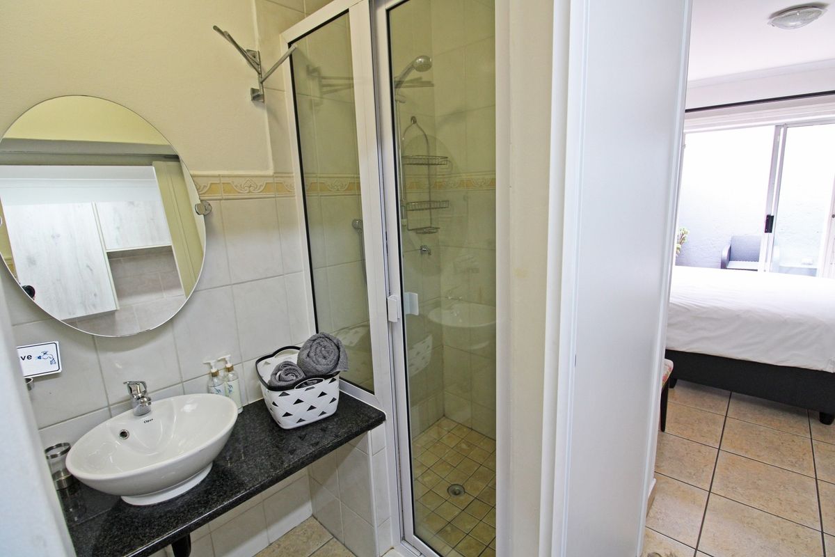 Compact bathroom featuring a vessel sink on a granite vanity, a glass-enclosed shower, and tiled flooring, with direct access to the adjacent bedroom.