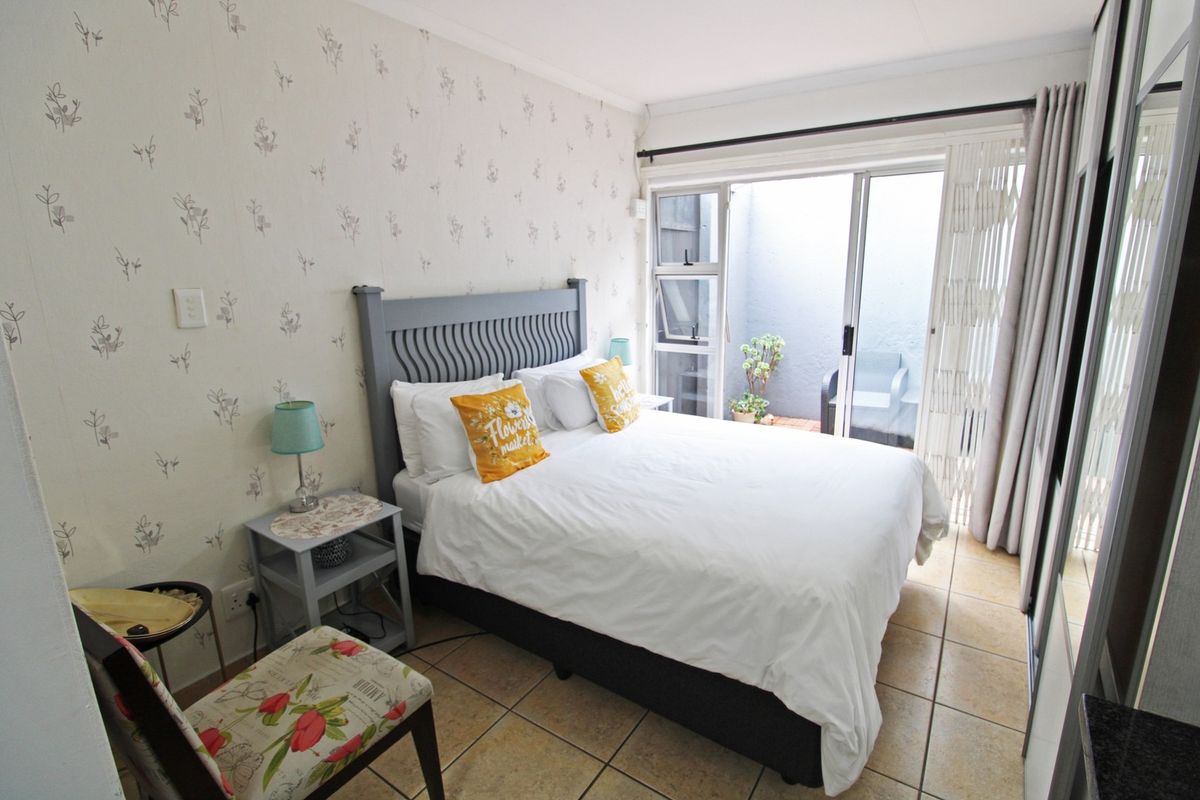 A cozy bedroom featuring tiled flooring, patterned wallpaper, and a sliding glass door providing access to a small private outdoor area.