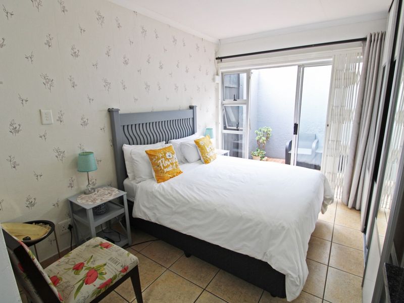 A cozy bedroom featuring tiled flooring, patterned wallpaper, and a sliding glass door providing access to a small private outdoor area.