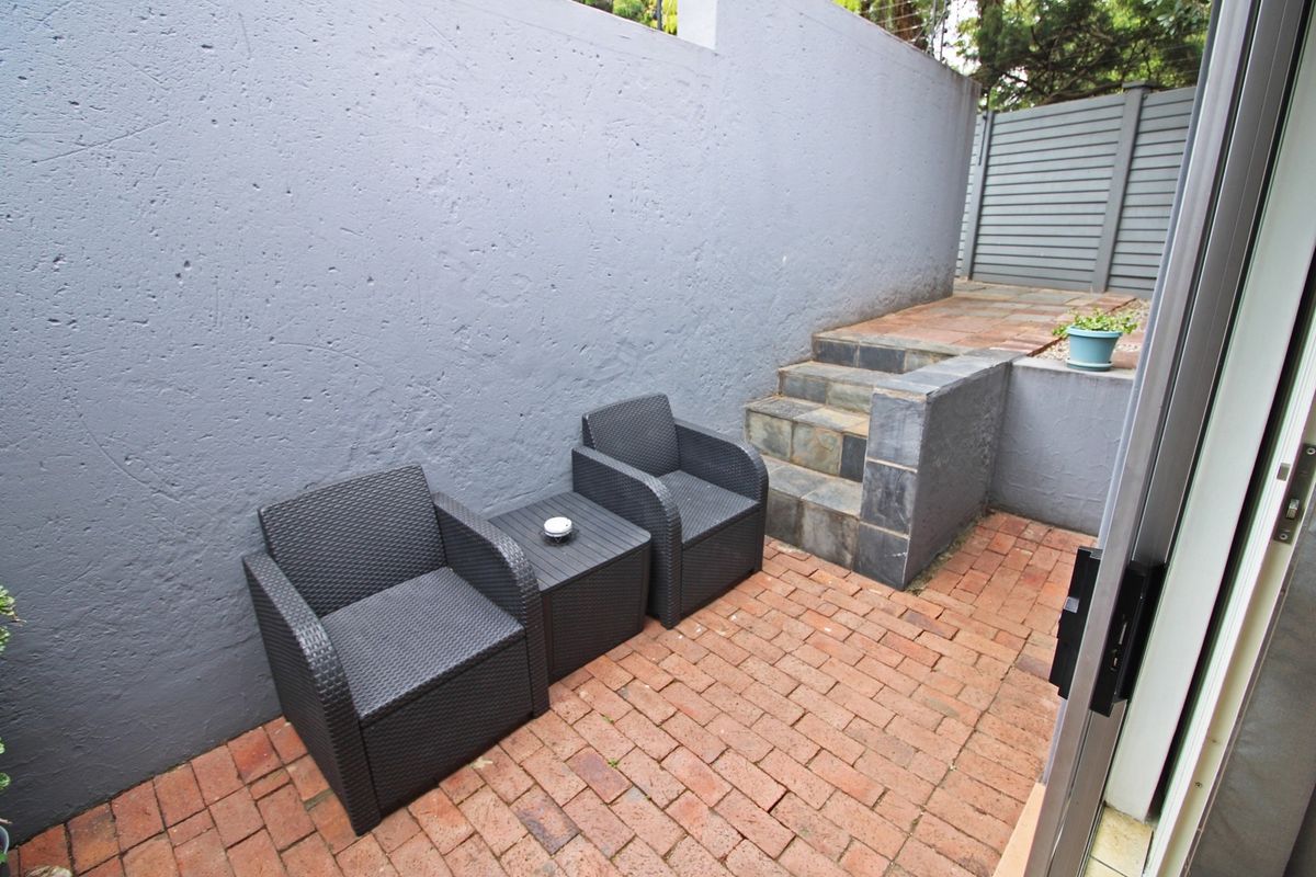 A private outdoor patio area featuring brick paving, stone steps, and a high boundary wall, providing a secluded space for relaxation.