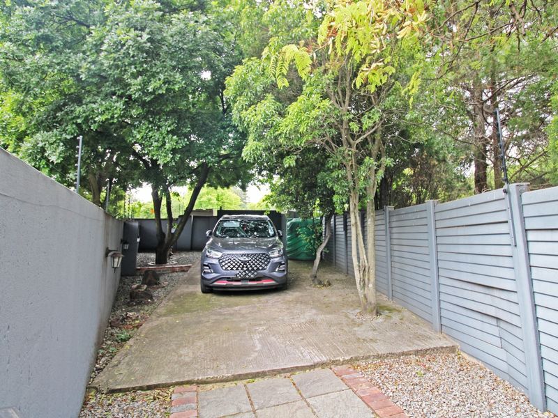 A private driveway entrance featuring a concrete parking area, enclosed by a combination of solid perimeter walls and timber slat fencing with electric security.