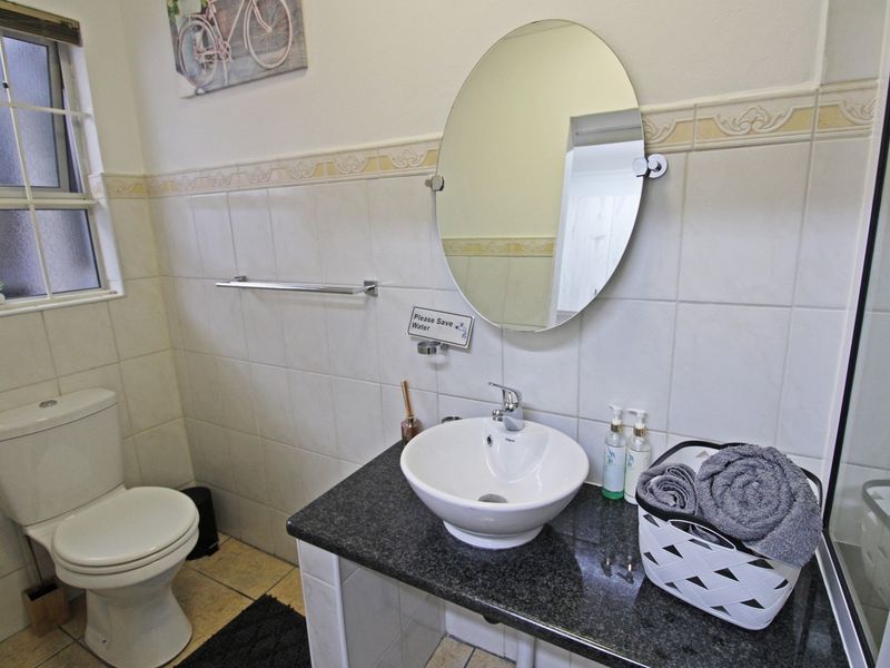 A functional bathroom featuring a vessel sink on a granite vanity, ceramic toilet, and neutral wall tiling with a decorative border.
