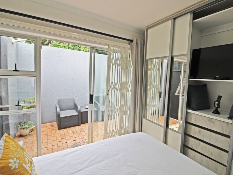 A bright bedroom featuring a built-in wardrobe and a sliding glass door that opens onto a private brick-paved patio area.