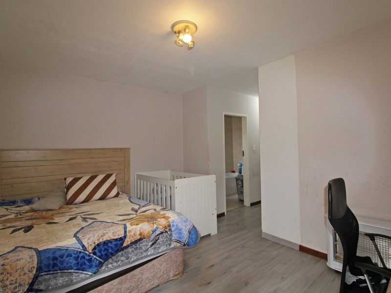 A bedroom featuring laminate flooring and a ceiling light fixture, with an adjoining space visible through the doorway.