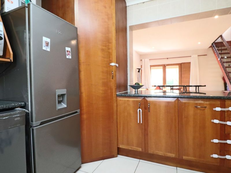 A functional kitchen featuring warm wooden cabinetry, granite countertops, and tiled flooring, with an open-plan layout connecting to the living area.