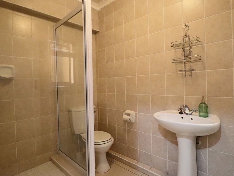 A functional bathroom featuring a pedestal sink, toilet, and a glass-enclosed shower with neutral ceramic wall tiling throughout.