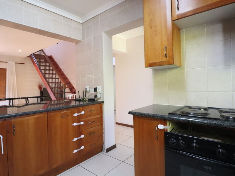 A functional kitchen featuring wooden cabinetry, granite countertops, and a built-in oven with hob, opening into the living area with a staircase visible.