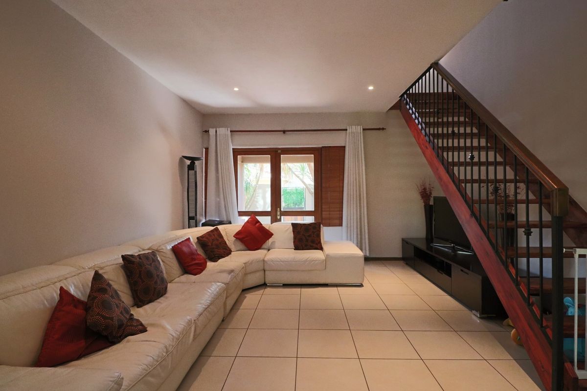 Spacious living room featuring tiled flooring, recessed lighting, and a timber staircase with a metal balustrade, leading to a set of french doors.
