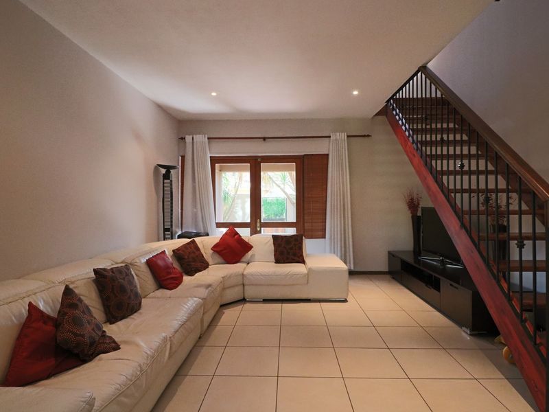 Spacious living room featuring tiled flooring, recessed lighting, and a timber staircase with a metal balustrade, leading to a set of french doors.
