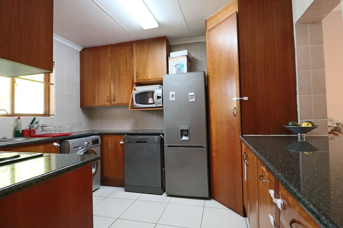 A functional kitchen featuring wood-finish cabinetry, granite countertops, tiled backsplash, and tiled flooring, offering ample storage and workspace.