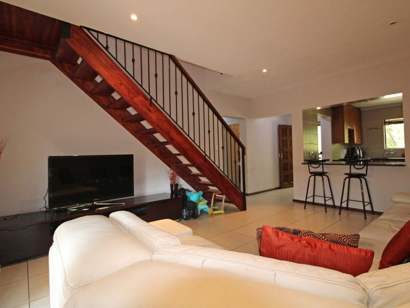 Open plan living area featuring a wooden staircase with wrought iron balustrade, tiled flooring, and a breakfast bar overlooking the kitchen.