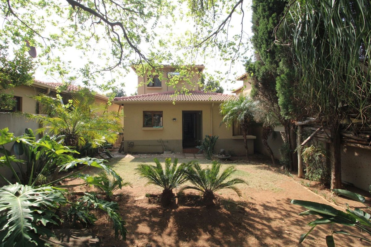 Rear view of the townhouse featuring a private garden, tiled patio area, and established landscaping with mature trees and shrubs.