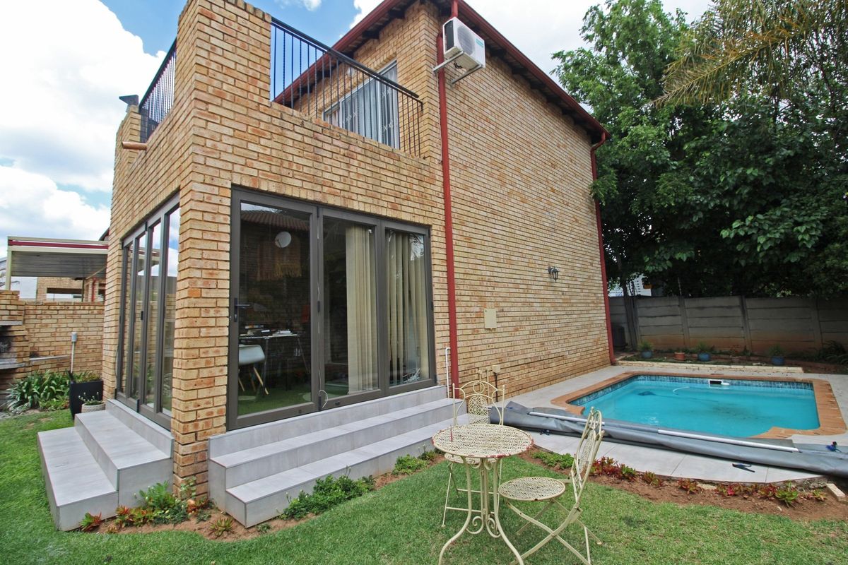Rear view of a double-story townhouse featuring a face brick exterior, a private swimming pool, and an upper-level balcony with metal railings.