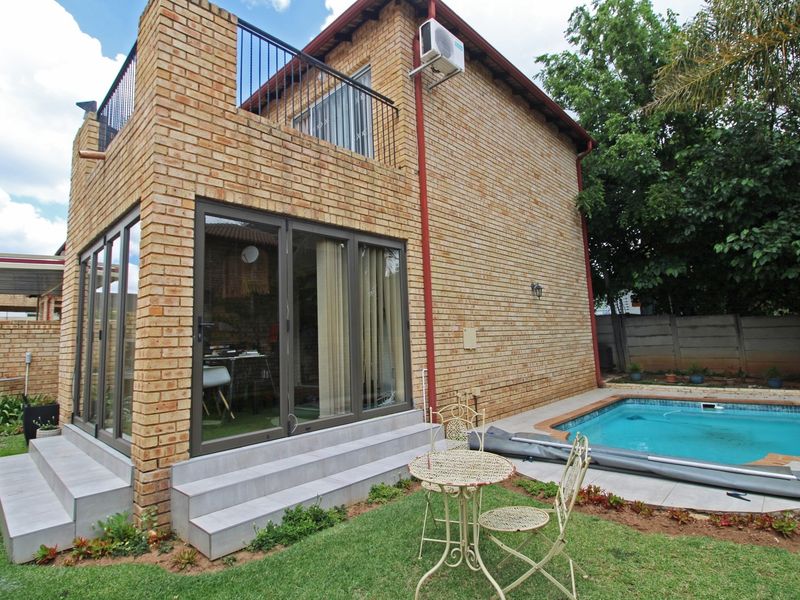 Rear view of a double-story townhouse featuring a face brick exterior, a private swimming pool, and an upper-level balcony with metal railings.