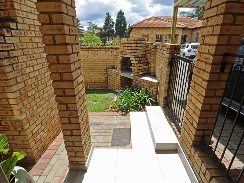 A private outdoor patio area featuring a built-in brick braai, paved flooring, and tiled steps, enclosed by brick boundary walls and a security gate.