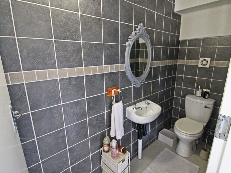 A compact bathroom featuring dark grey wall tiles, a wall-mounted basin, and a standard toilet.