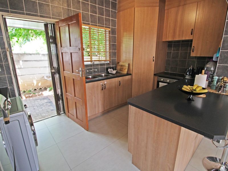 A functional kitchen featuring wood-finish cabinetry, dark laminate countertops, tiled backsplash, and direct access to an outdoor patio area.