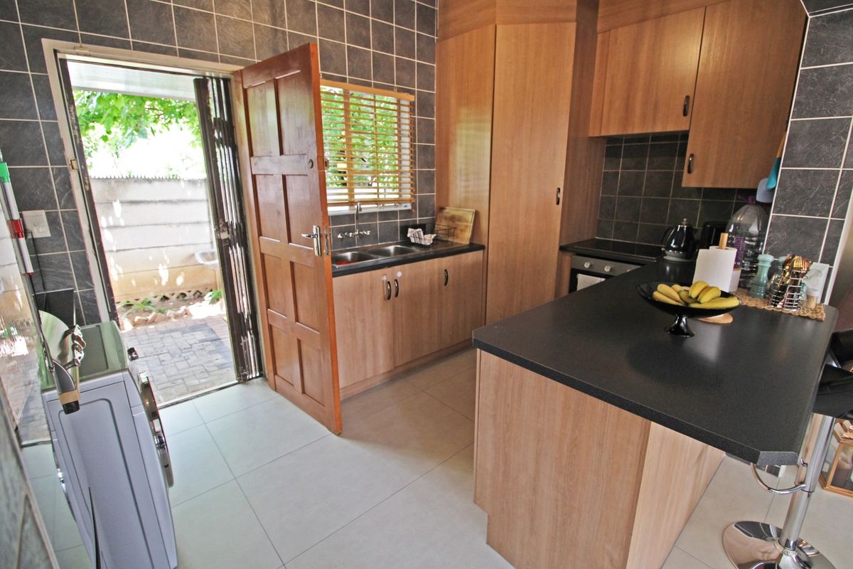 A functional kitchen featuring wood-finish cabinetry, dark laminate countertops, tiled backsplash, and direct access to an outdoor patio area.