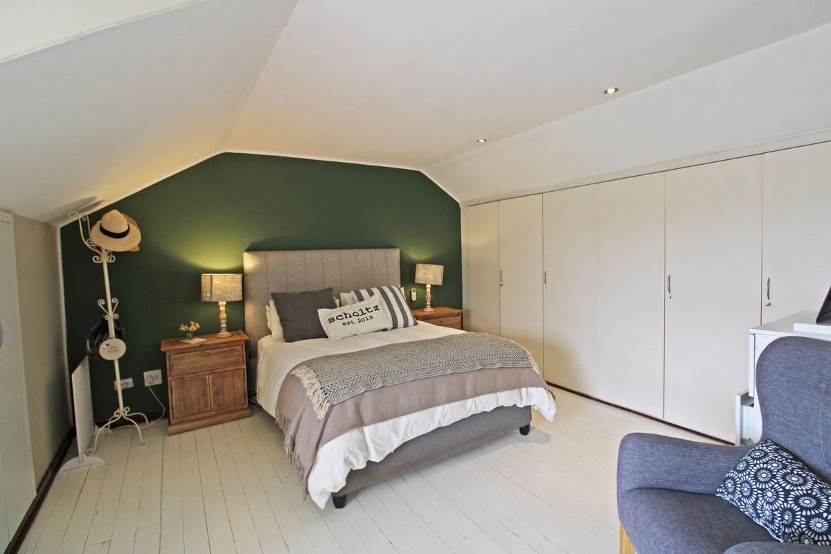 A well-lit bedroom featuring a sloped ceiling, built-in cupboards, and a feature wall, offering a comfortable and functional living space.