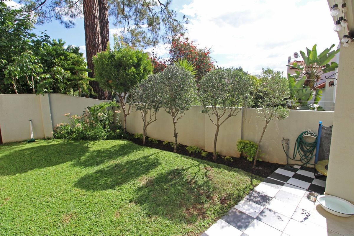 A private rear garden featuring a well-maintained lawn, landscaped trees along the boundary wall, and a tiled patio area.