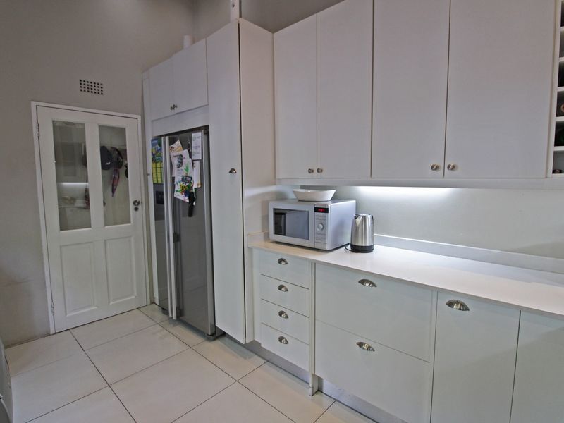 A clean, modern kitchen featuring white built-in cabinetry, stone countertops, under-cabinet lighting, and integrated wine storage with tiled flooring.