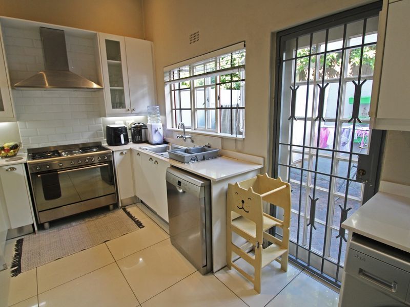 Modern kitchen featuring white cabinetry, subway tile backsplash, stainless steel gas stove, and direct access to the rear patio through a secure door.