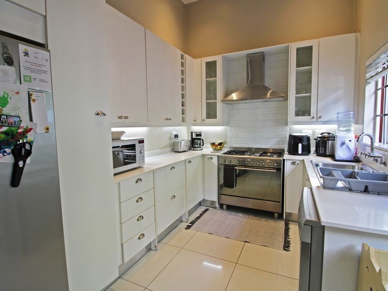 Modern kitchen featuring white cabinetry, subway tile backsplash, stainless steel gas stove with extractor fan, and tiled flooring.