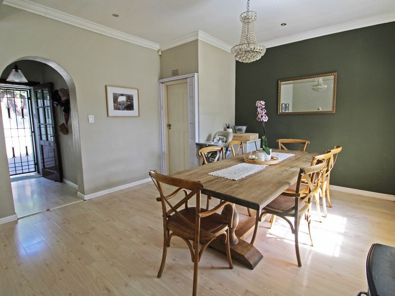 A well-lit dining room featuring laminate flooring, crown molding, and a decorative crystal chandelier, with an arched entryway leading to the home's entrance.