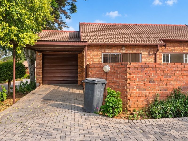 Front exterior view of a brick townhouse featuring a paved driveway, covered carport, and secure roller garage door.