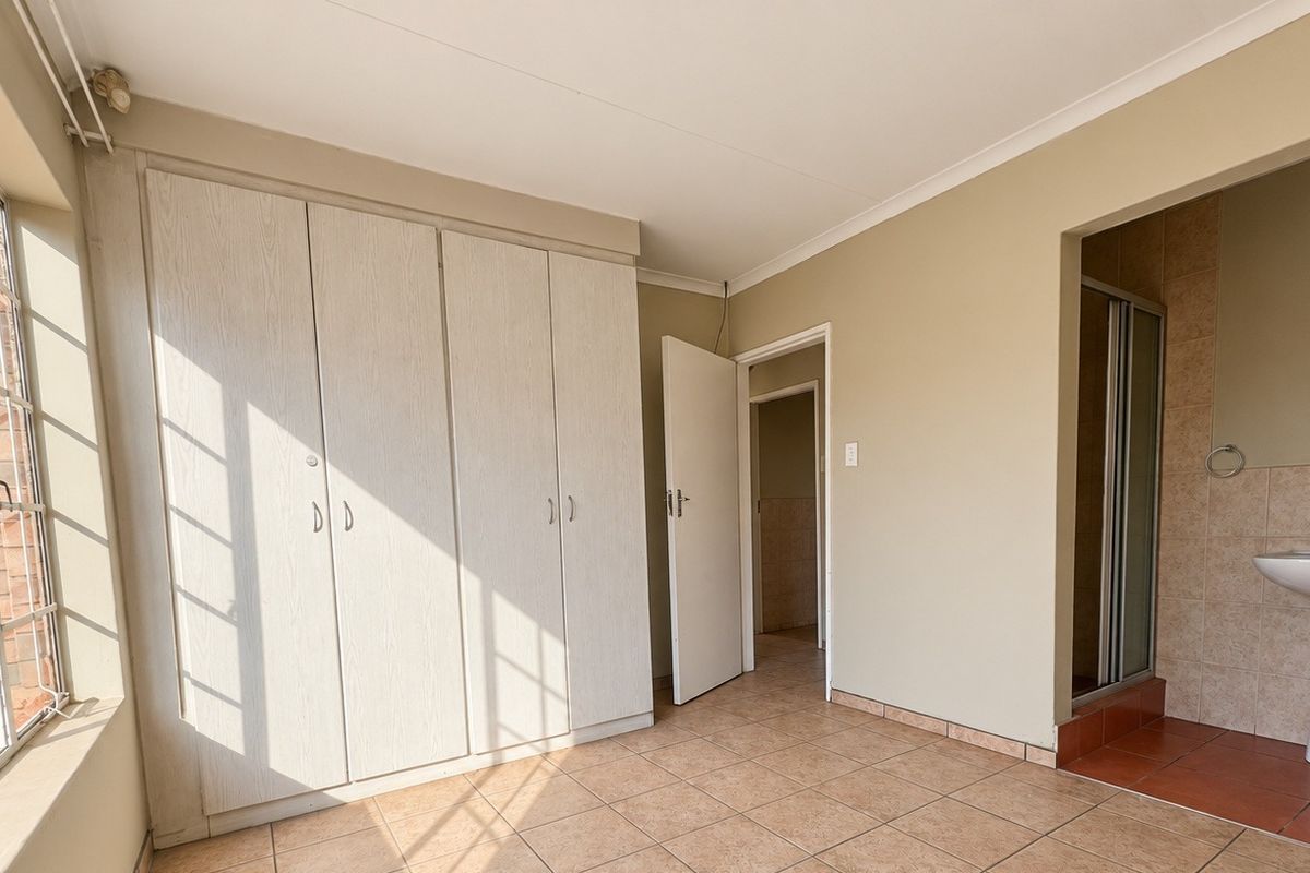 A spacious bedroom featuring built-in cupboards, tiled flooring, and an en-suite bathroom with a pedestal basin and shower enclosure.